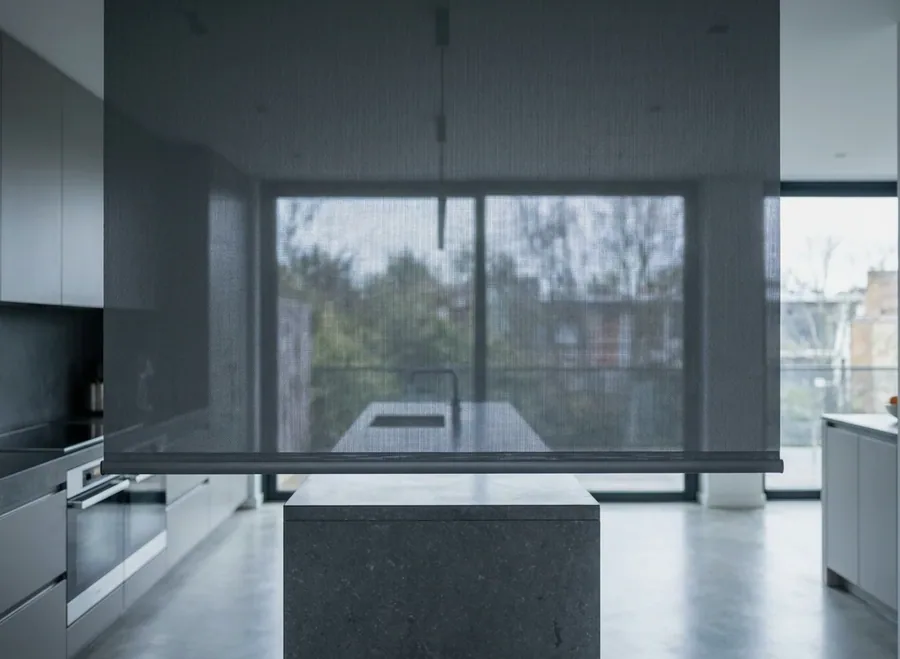 Sunscreen roller blind lowered over a garden-facing window — one smooth fabric panel, no folds